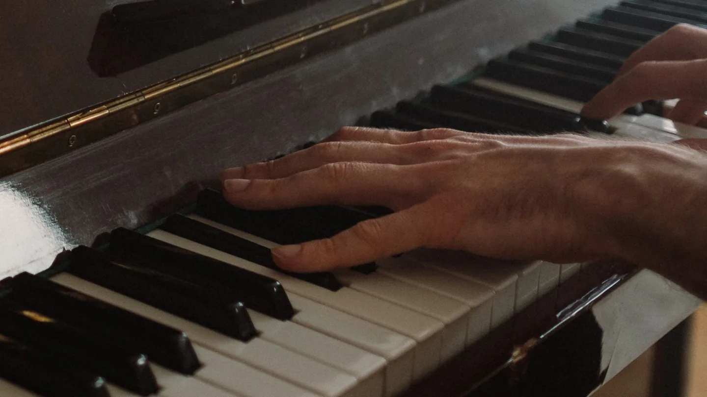 Hands playing the keys of an upright piano.