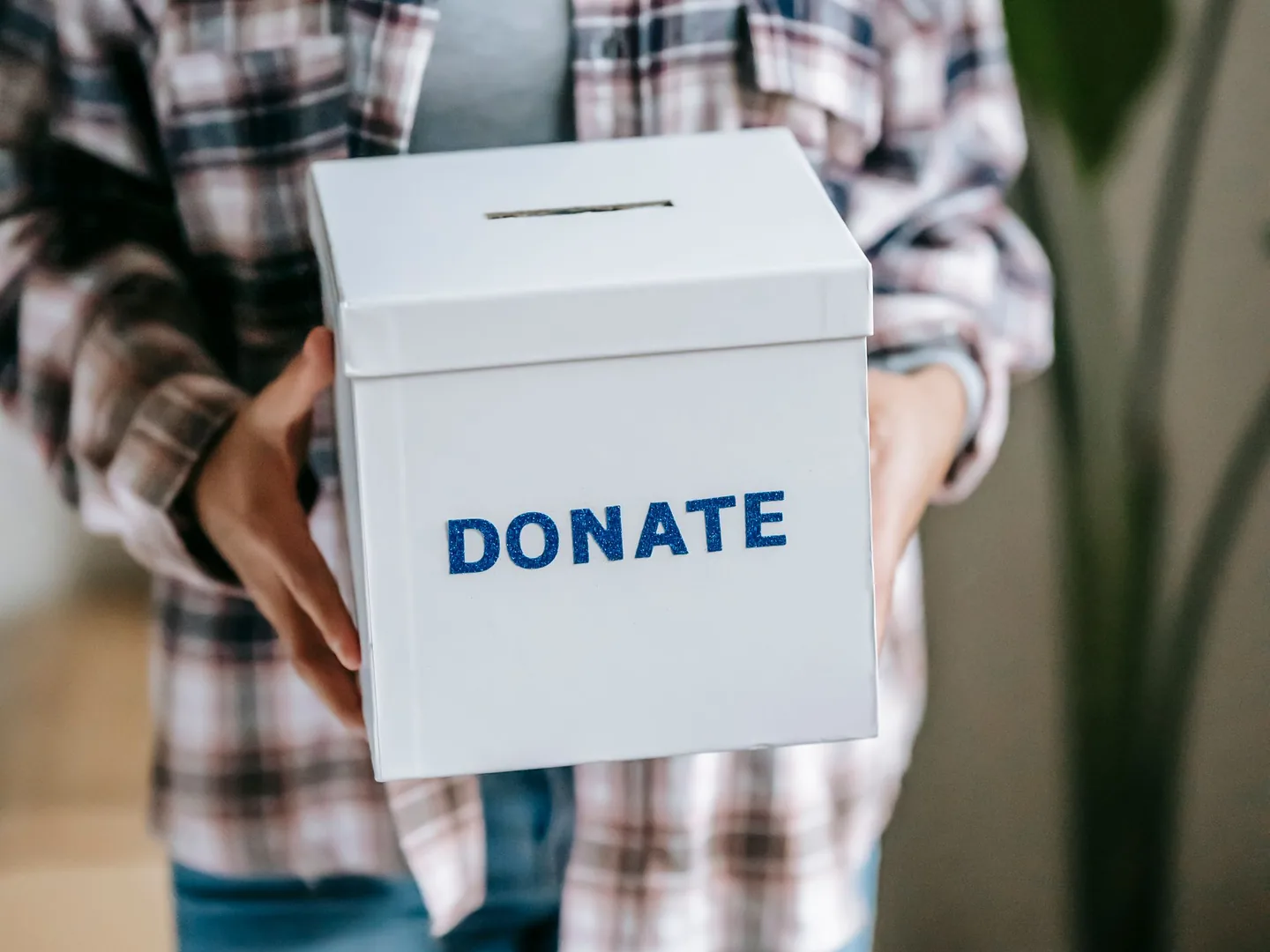 Hands holding a white collection box marked “DONATE”.
