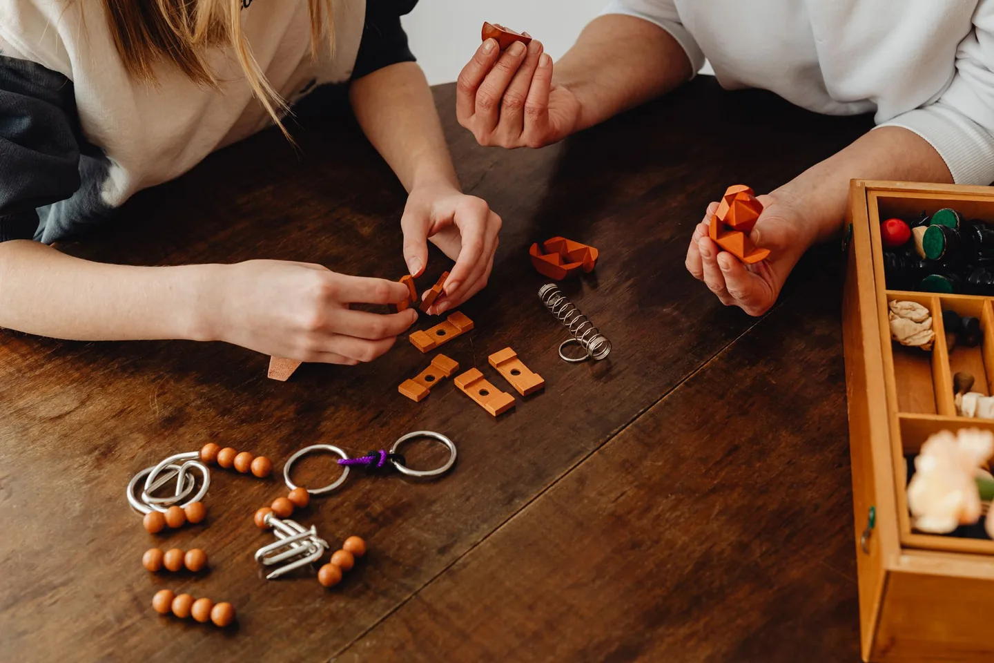 Hands working on wooden puzzles at a shared table.