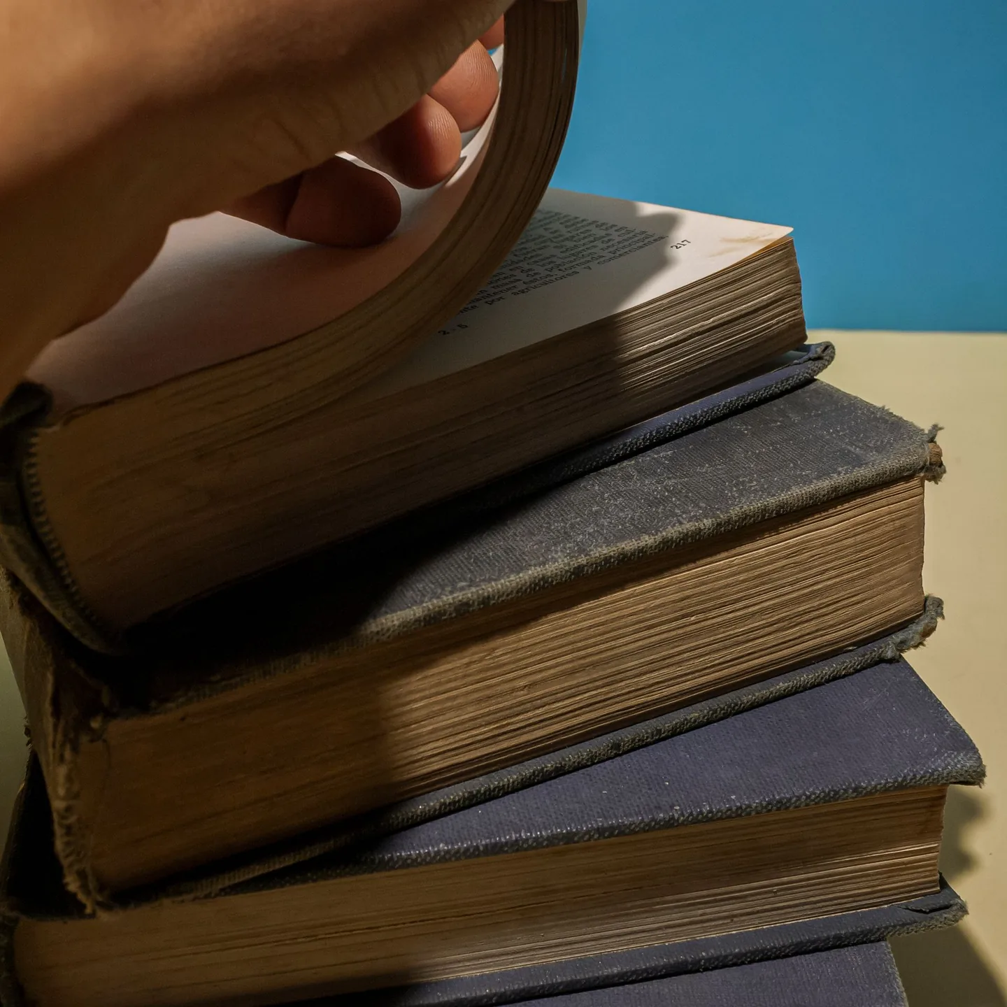 A hand turns pages in a stack of worn, clothbound books.