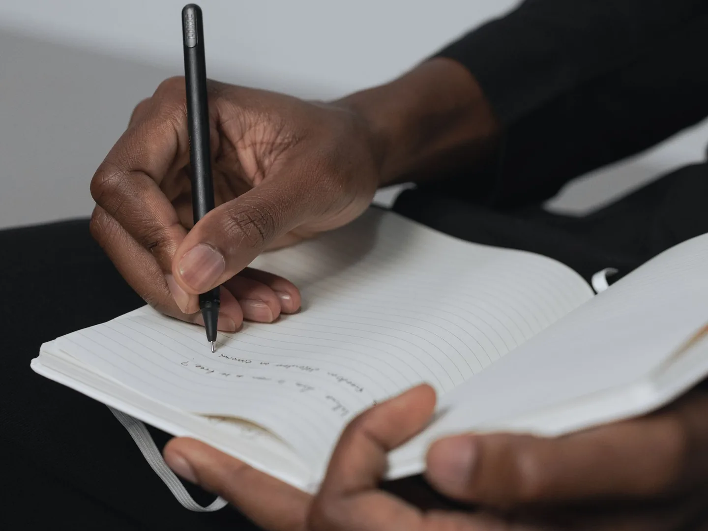 Hands writing with a pen in a lined notebook.